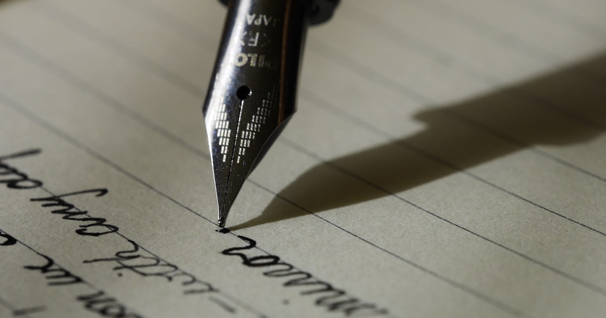 Open notebook and pen on a wooden desk beside a window